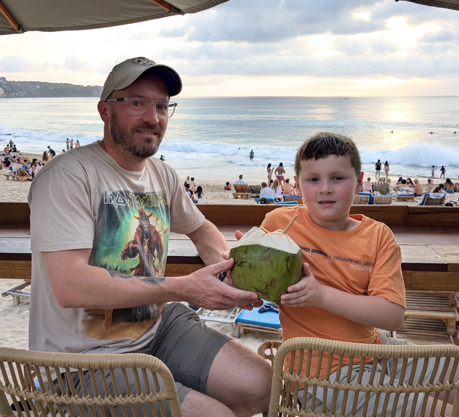 Jim and his son sharing a coconut on a Bali beach at sunset